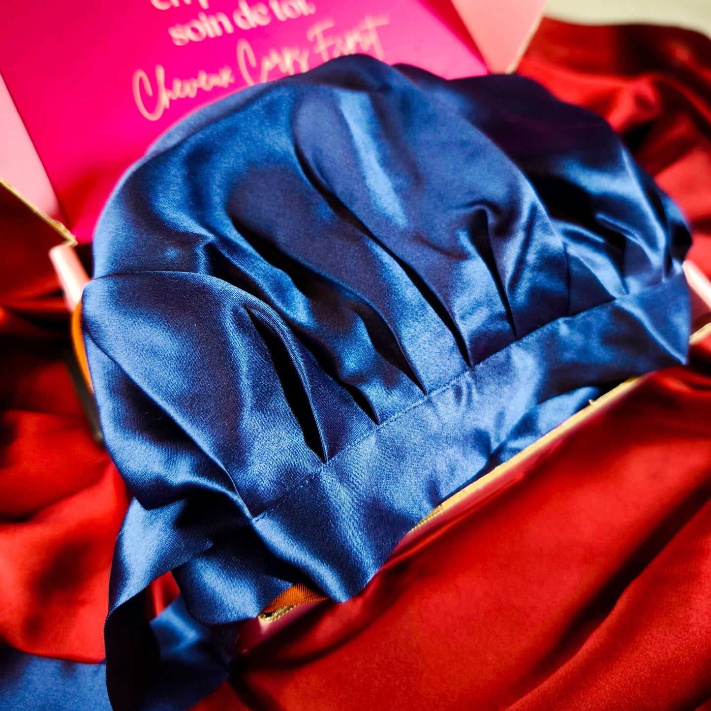 Bonnet en soie bleu nuit présenté sur fond rouge, plié dans son emballage